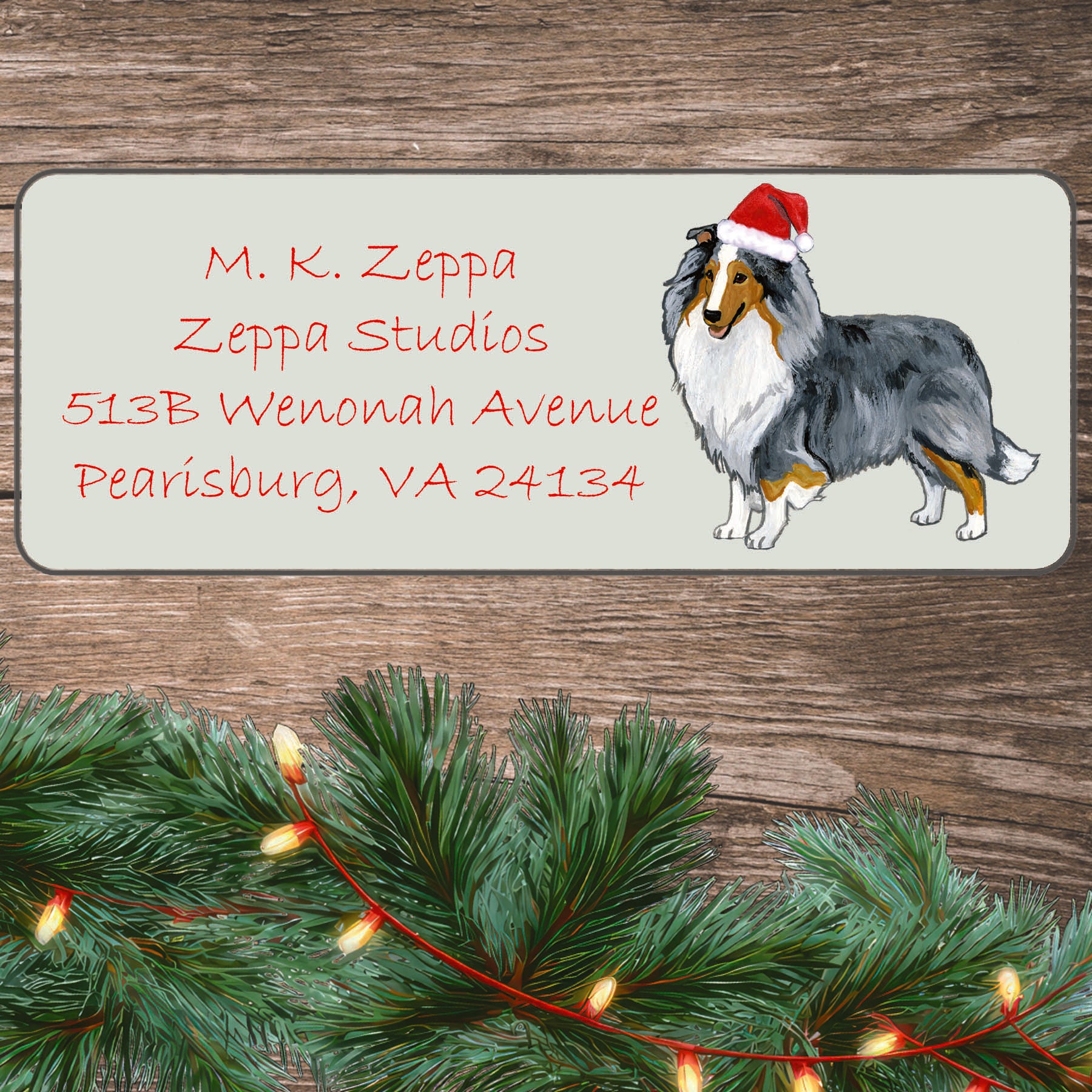 An illustration of a blue merle Shetland Sheepdog wearing a Santa Hat on an ivory return address label set off by a wood surface with holiday greenery background.