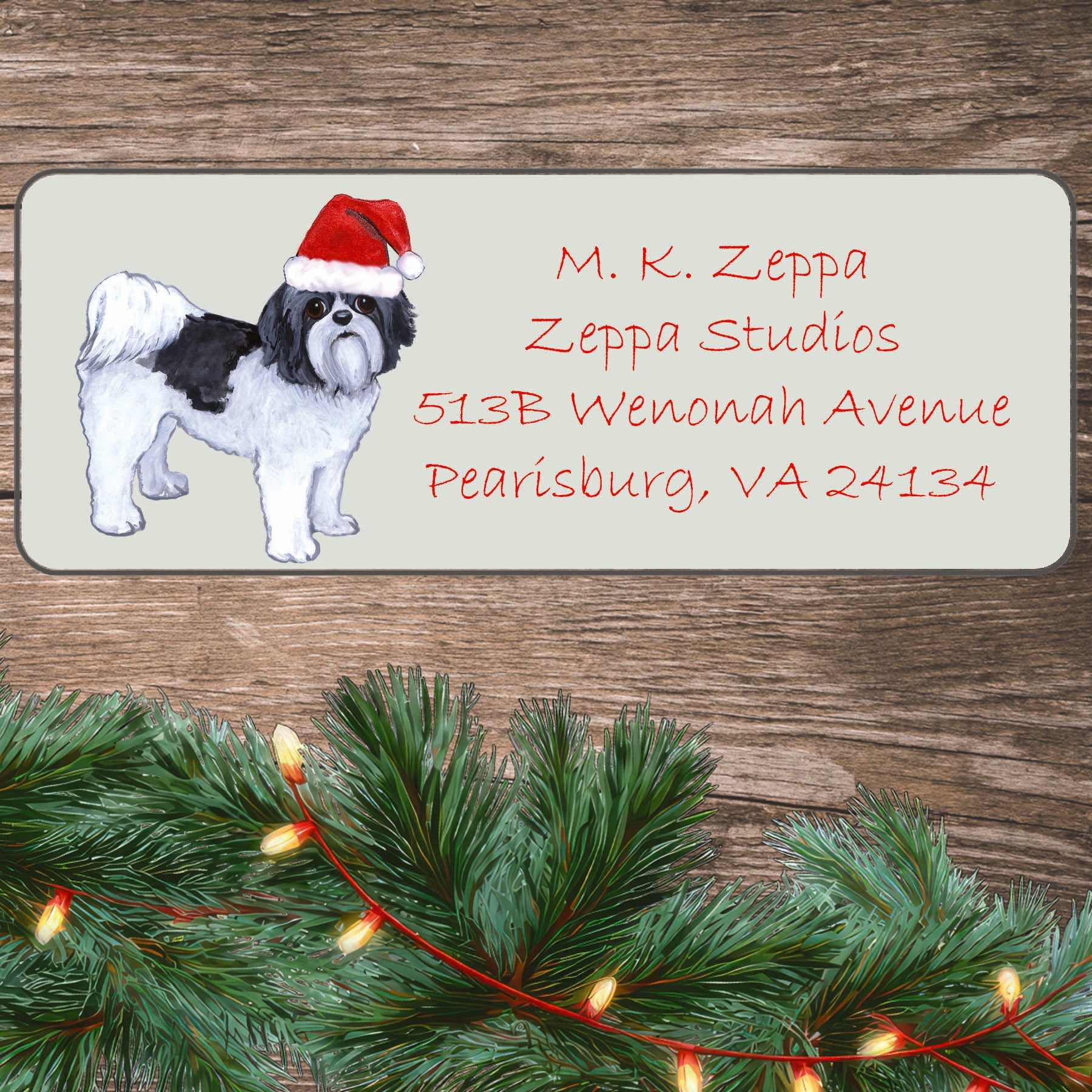 An illustration of a Shih Tzu with a puppy clip wearing a Santa Hat on an ivory return address label set off by a wood surface with holiday greenery background.