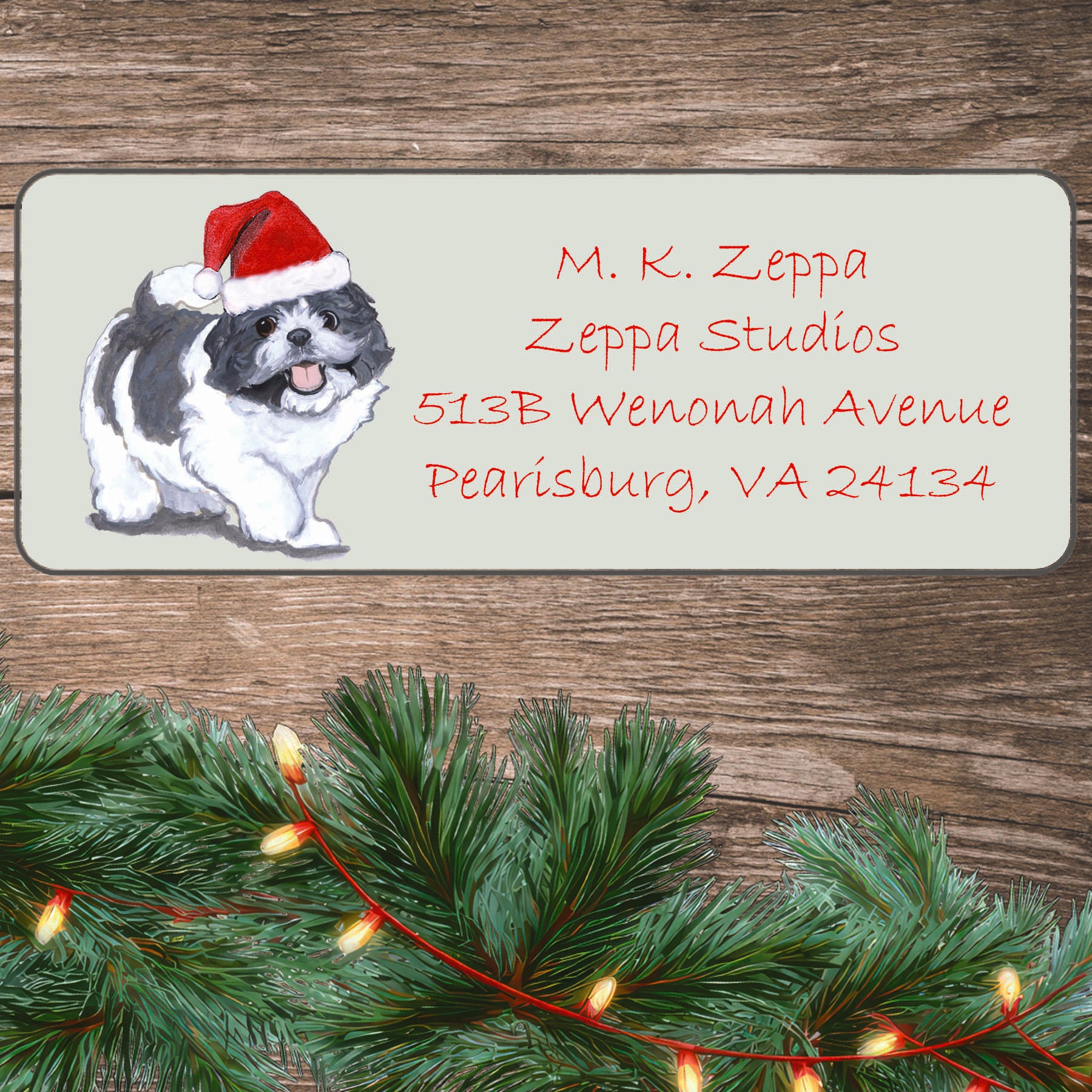 An illustration of a Shih Tzu puppy wearing a Santa Hat on an ivory return address label set off by a wood surface with holiday greenery background.