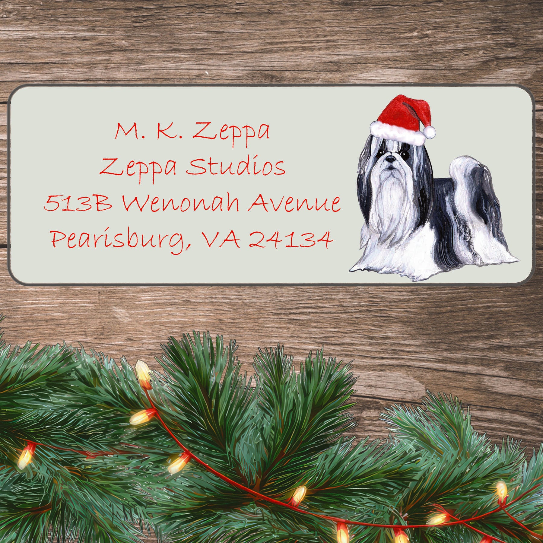 An illustration of a Shih Tzu wearing a Santa Hat on an ivory return address label set off by a wood surface with holiday greenery background.