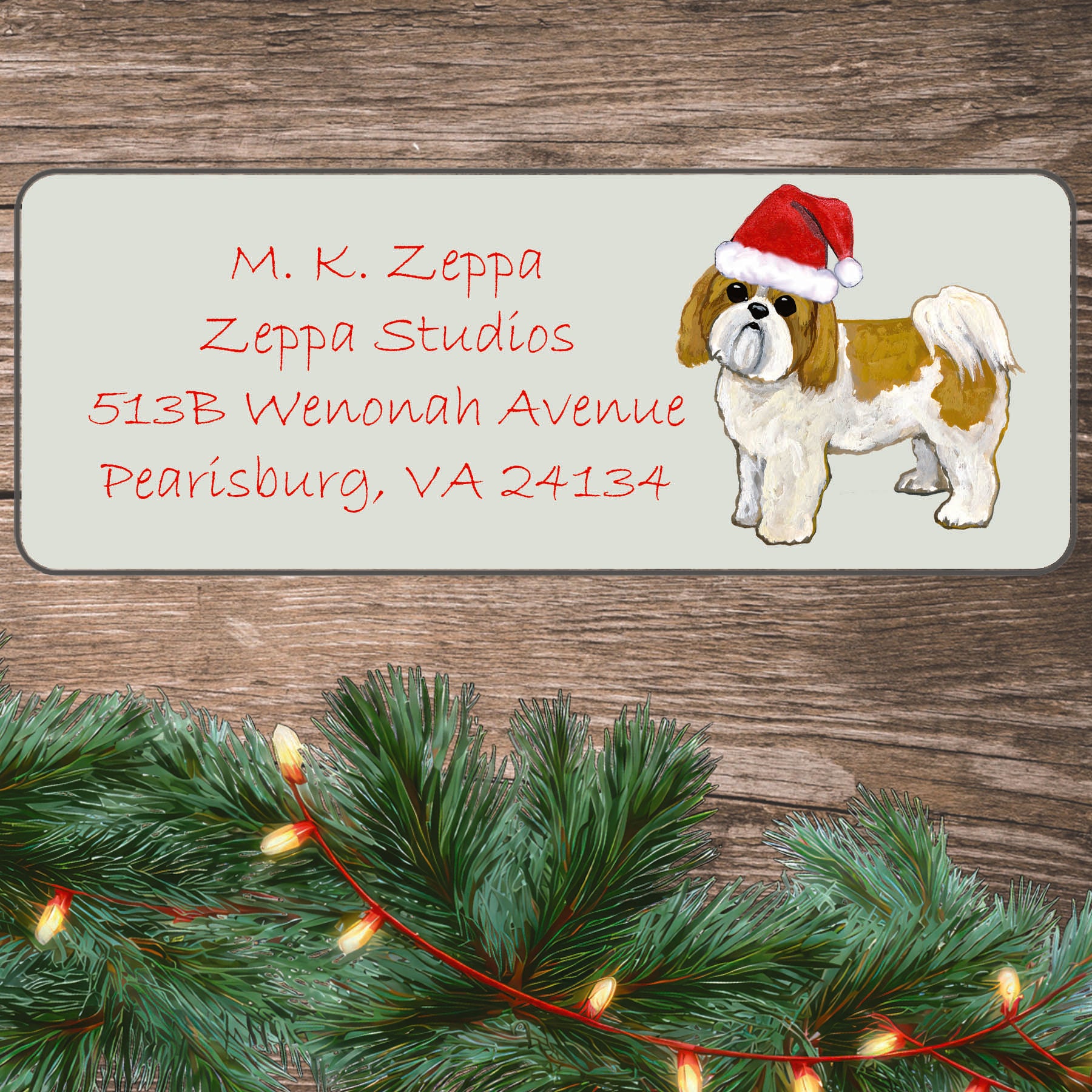 An illustration of a tan and white Shih Tzu with a puppy clip wearing a Santa Hat on an ivory return address label set off by a wood surface with holiday greenery background.