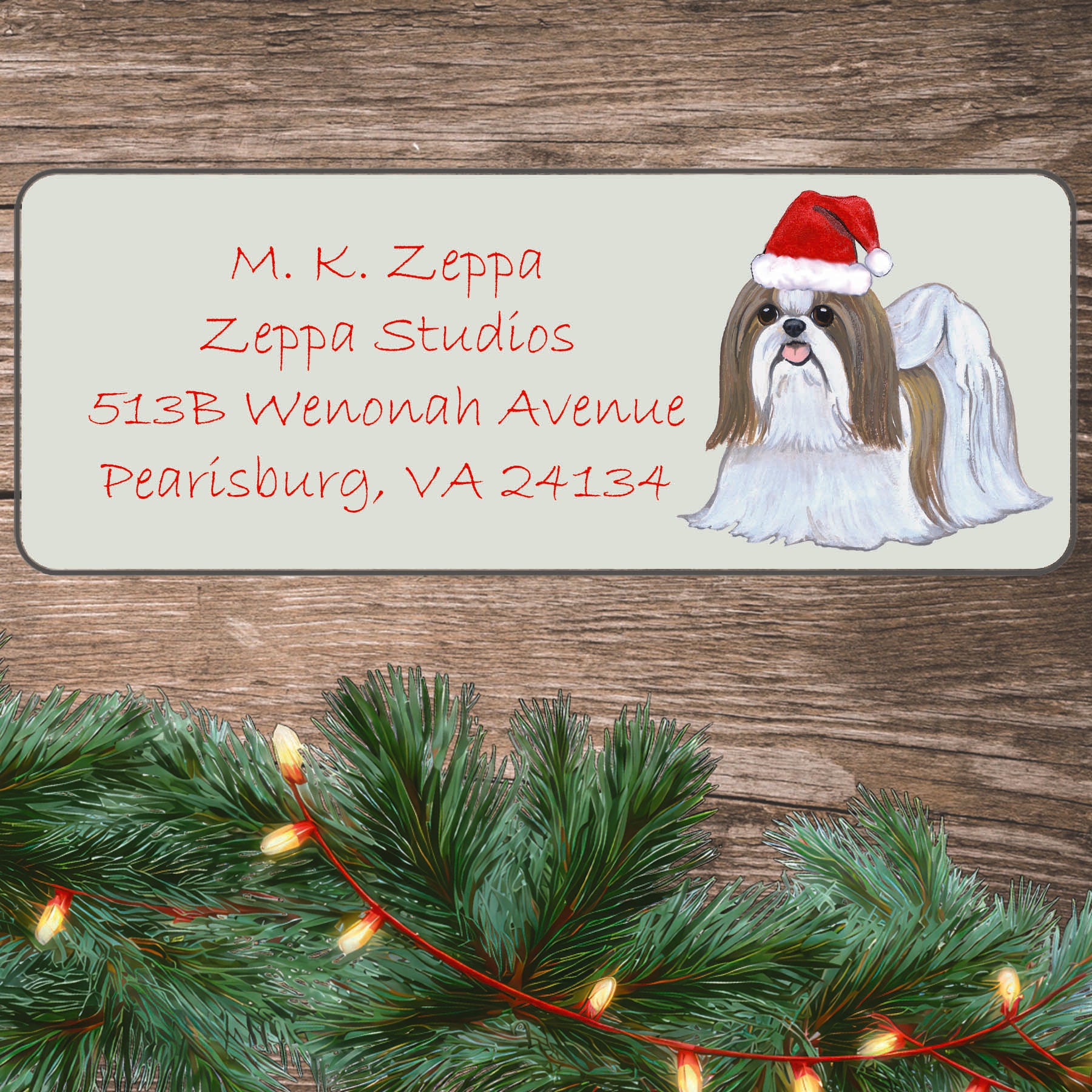 An illustration of a tan and white Shih Tzu wearing a Santa Hat on an ivory return address label set off by a wood surface with holiday greenery background.