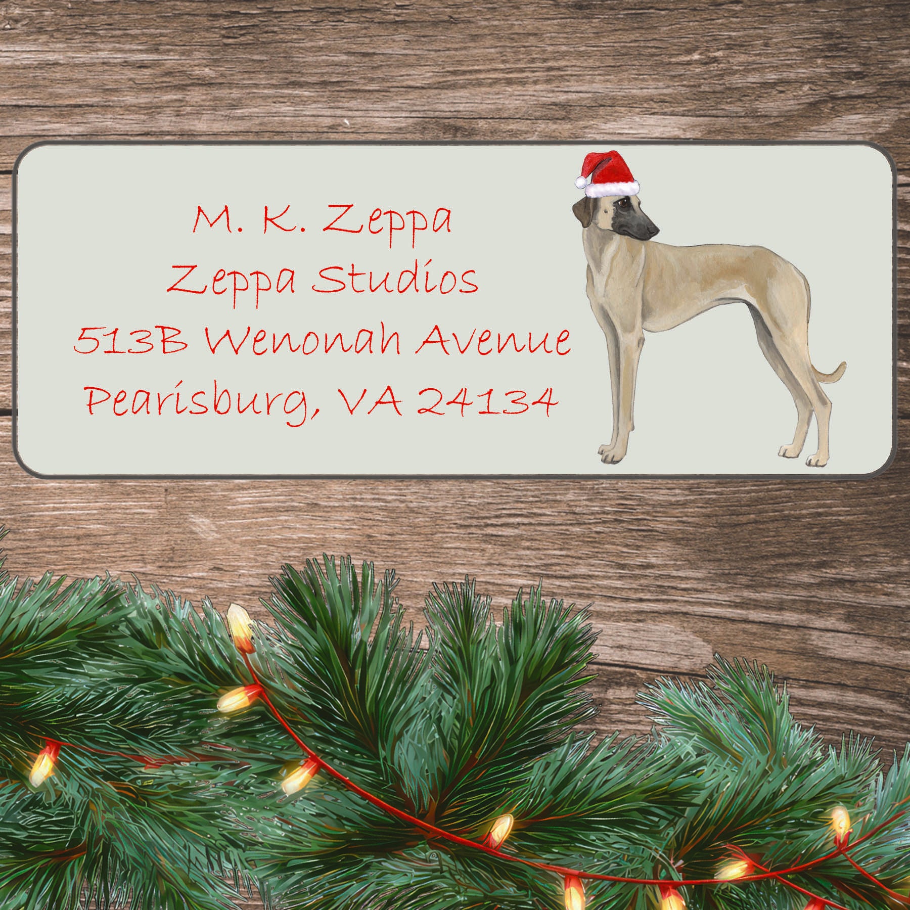 A Sloughi wearing a Santa Hat illustration on an ivory return address label set off by a wood surface with holiday greenery background.