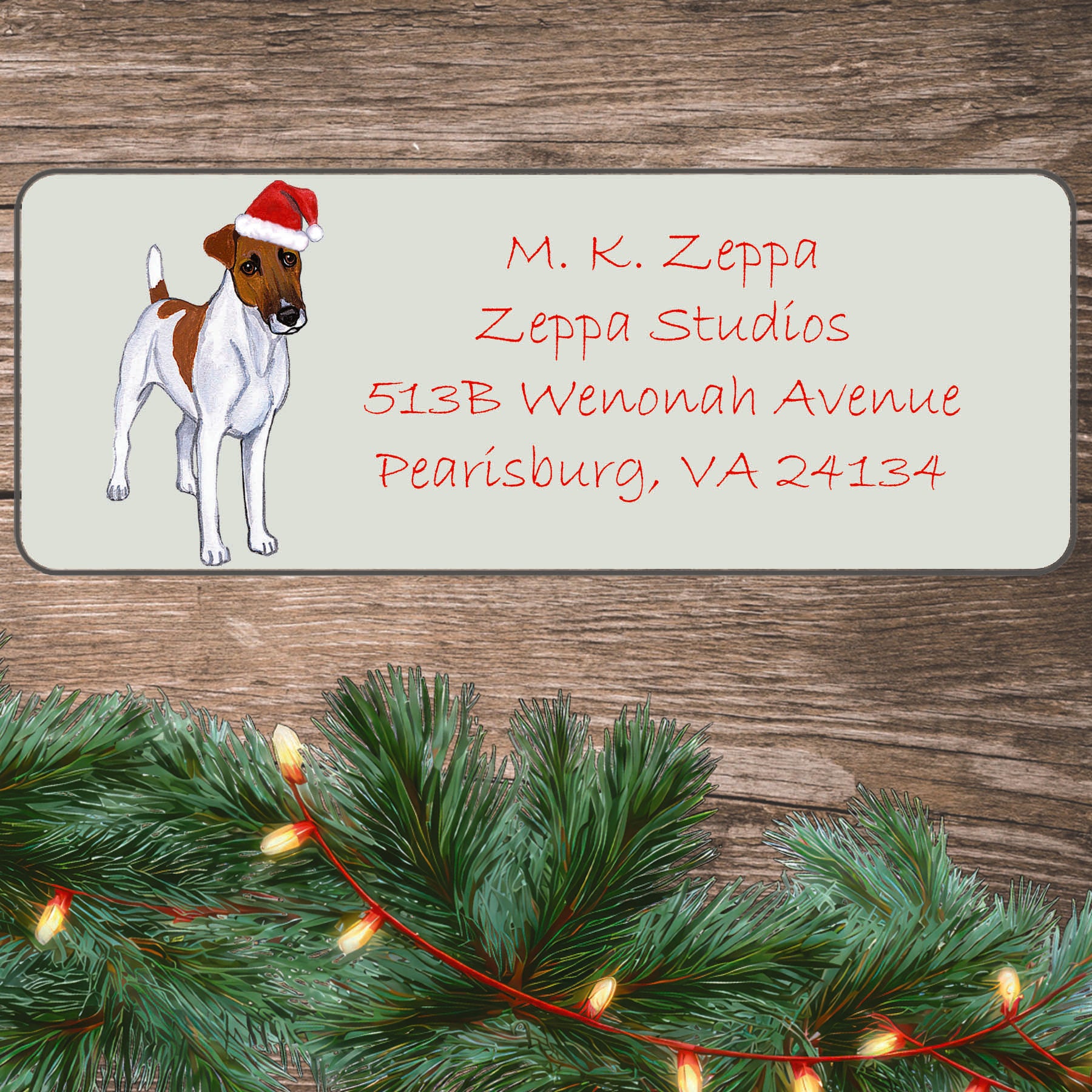 An illustration of a Smooth Fox Terrier wearing a Santa Hat on an ivory return address label set off by a wood surface with holiday greenery background.