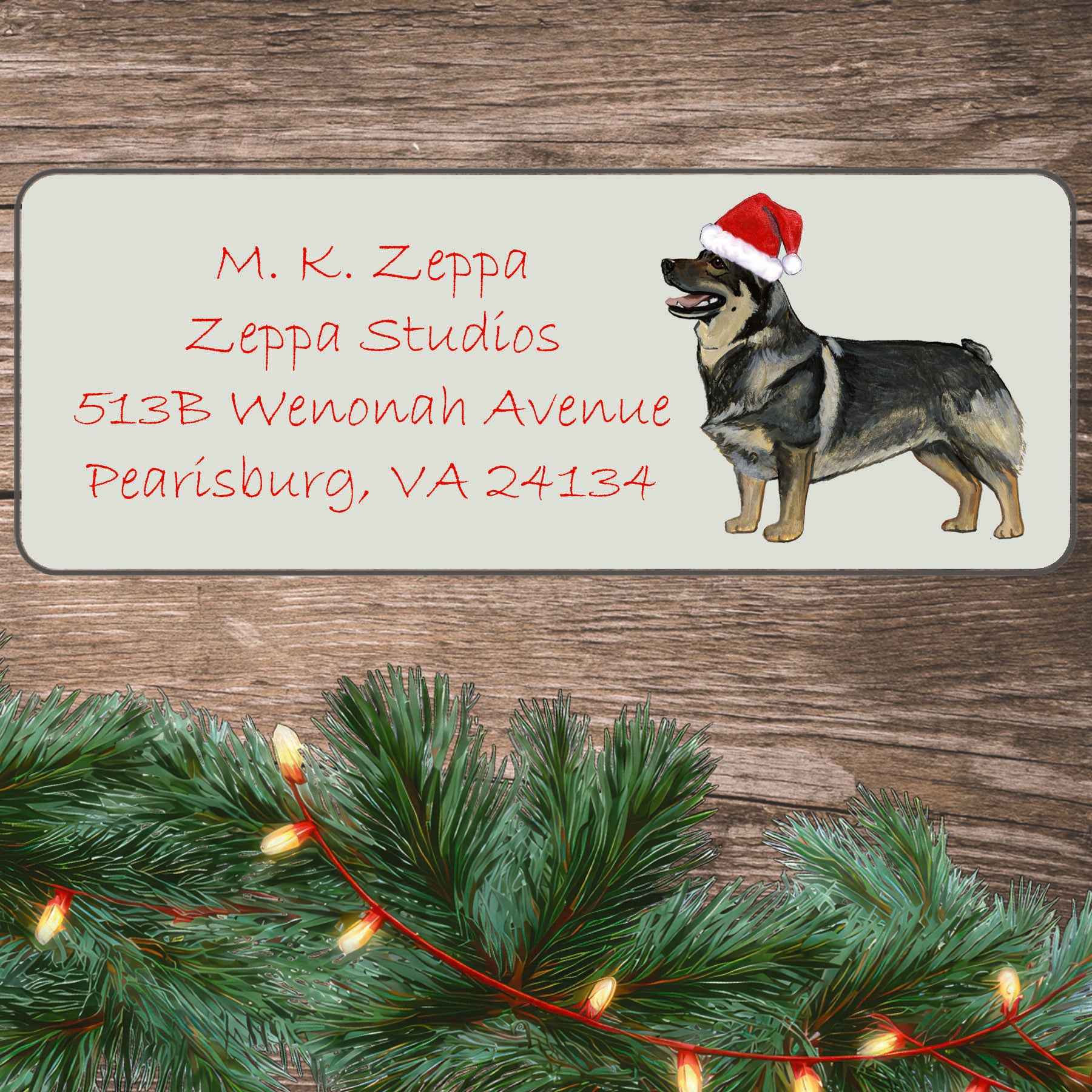 An illustration of a Swedish Vallhund wearing a Santa Hat on an ivory return address label set off by a wood surface with holiday greenery background.