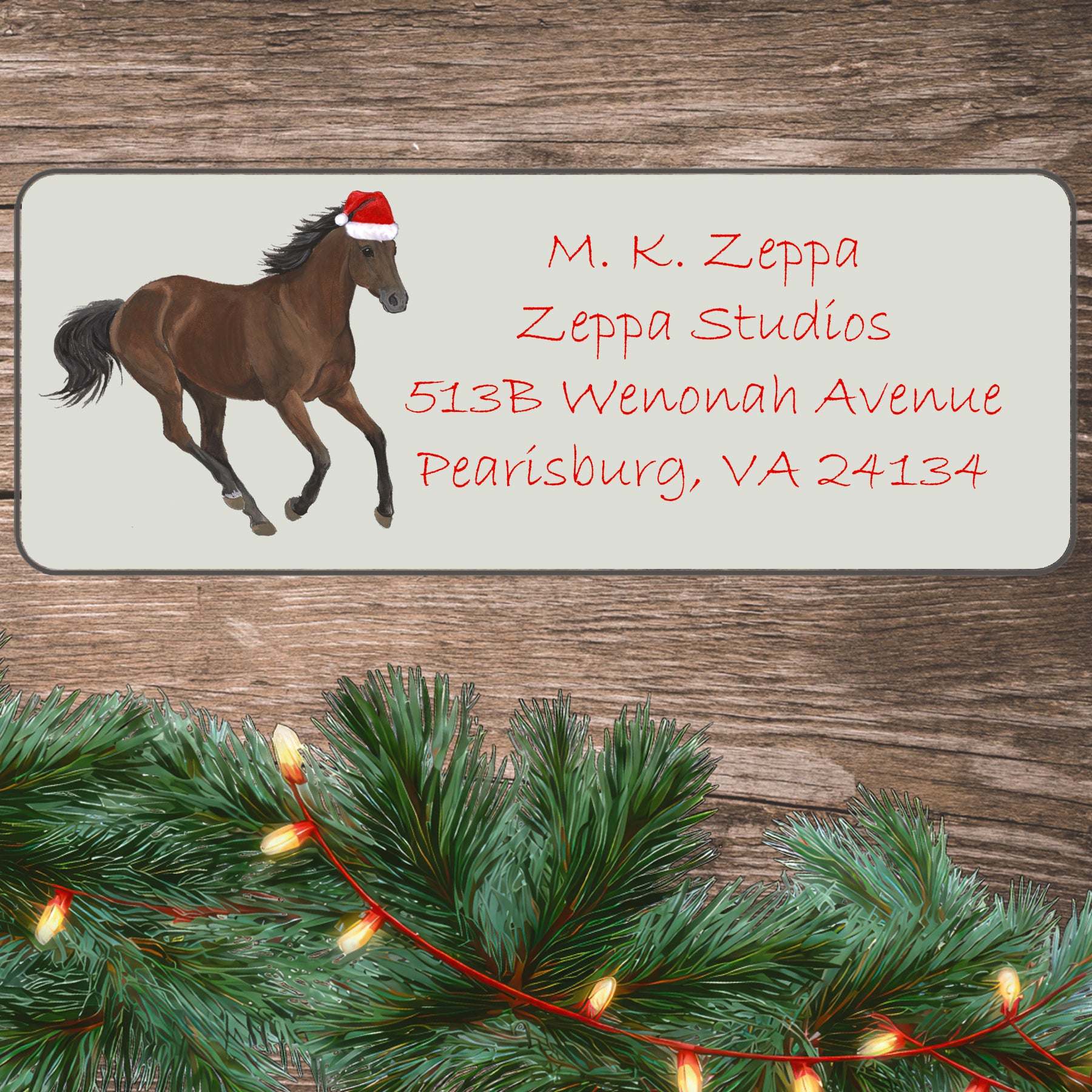 An illustration of a Thoroughbred horse wearing a Santa Hat on an ivory return address label set off by a wood surface with holiday greenery background.