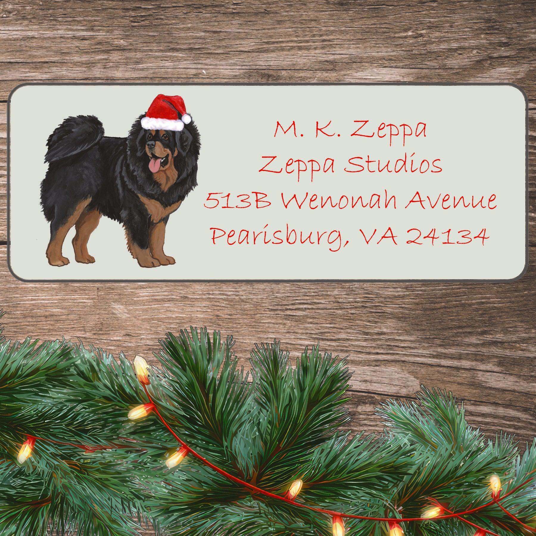 A Tibetan Mastiff in a Santa Hat illustration on an ivory return address label set off by a wood surface with holiday greenery background.