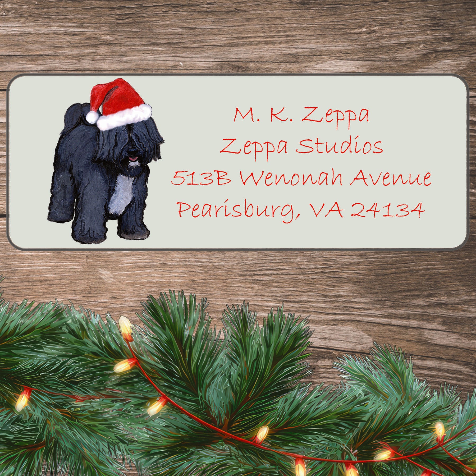 An illustration of a Tibetan Terrier wearing a Santa Hat on an ivory return address label set off by a wood surface with holiday greenery background.