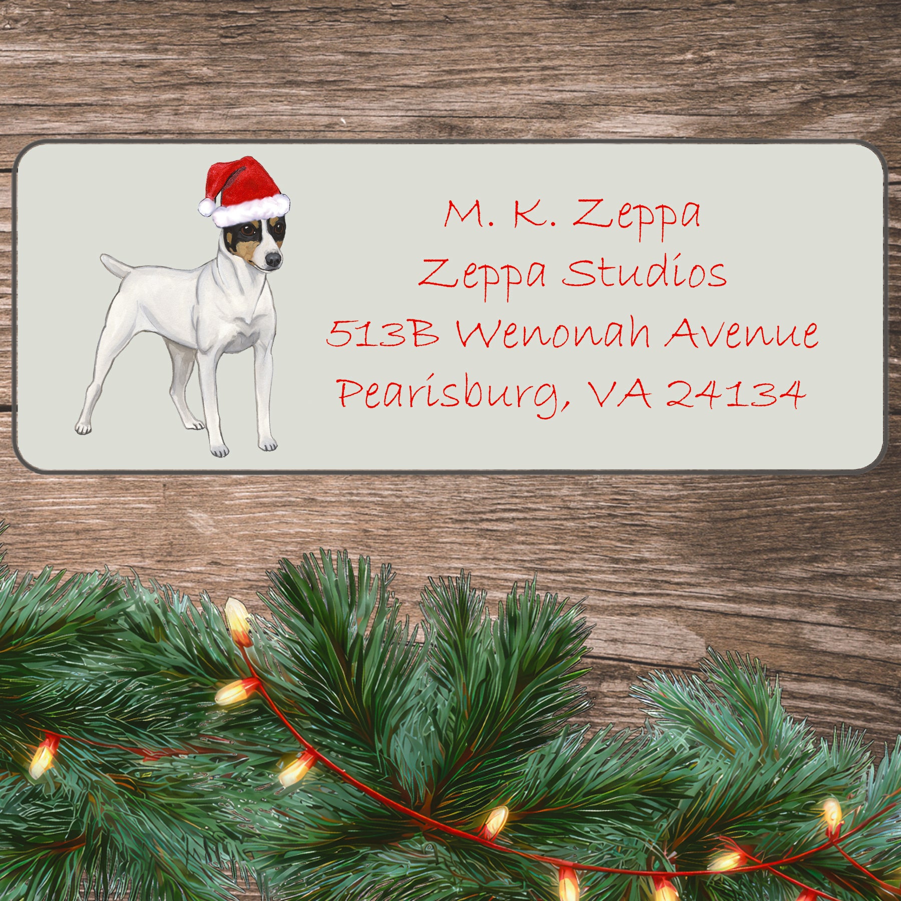 A Toy Fox Terrier in a Santa Hat illustration on an ivory return address label set off by a wood surface with holiday greenery background.