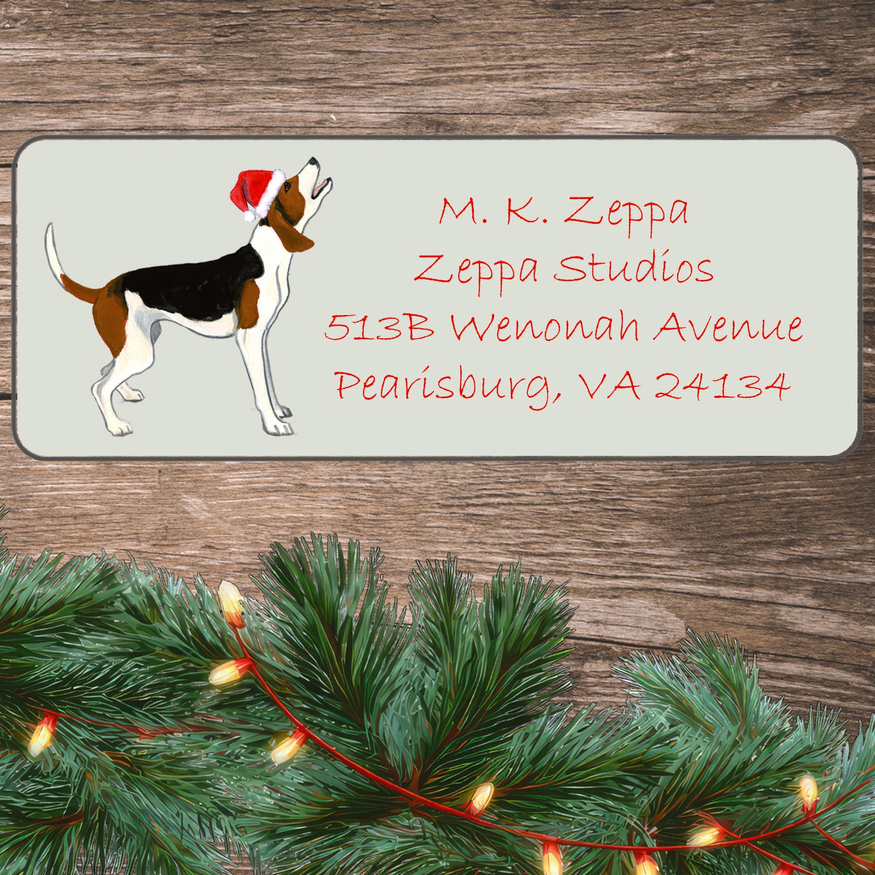 An illustration of a Treeing Walker Coonhound wearing a Santa Hat on an ivory return address label set off by a wood surface with holiday greenery background.