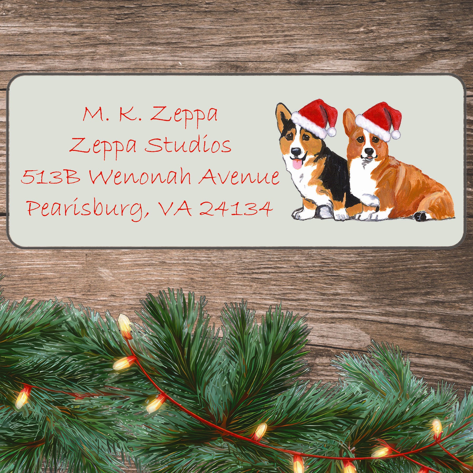 A pair of Pembroke Welsh Corgis in Santa Hatsillustration on an ivory return address label set off by a wood surface with holiday greenery background.