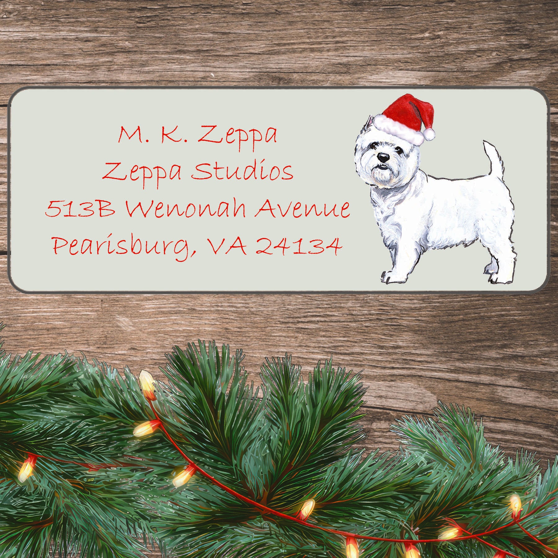 An illustration of a West Highland White Terrier wearing a Santa Hat on an ivory return address label set off by a wood surface with holiday greenery background.