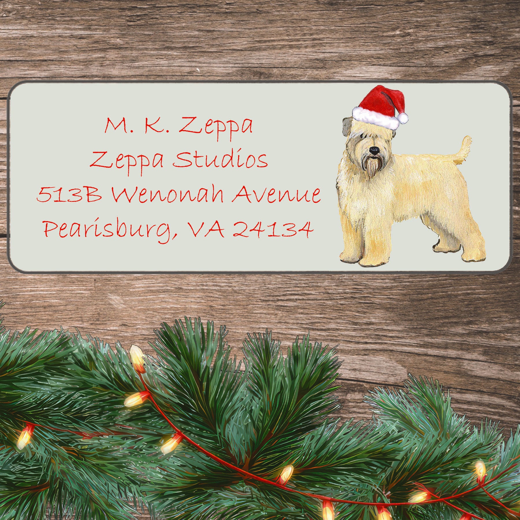 An illustration of a Wheaten Terrier wearing a Santa Hat on an ivory return address label set off by a wood surface with holiday greenery background.
