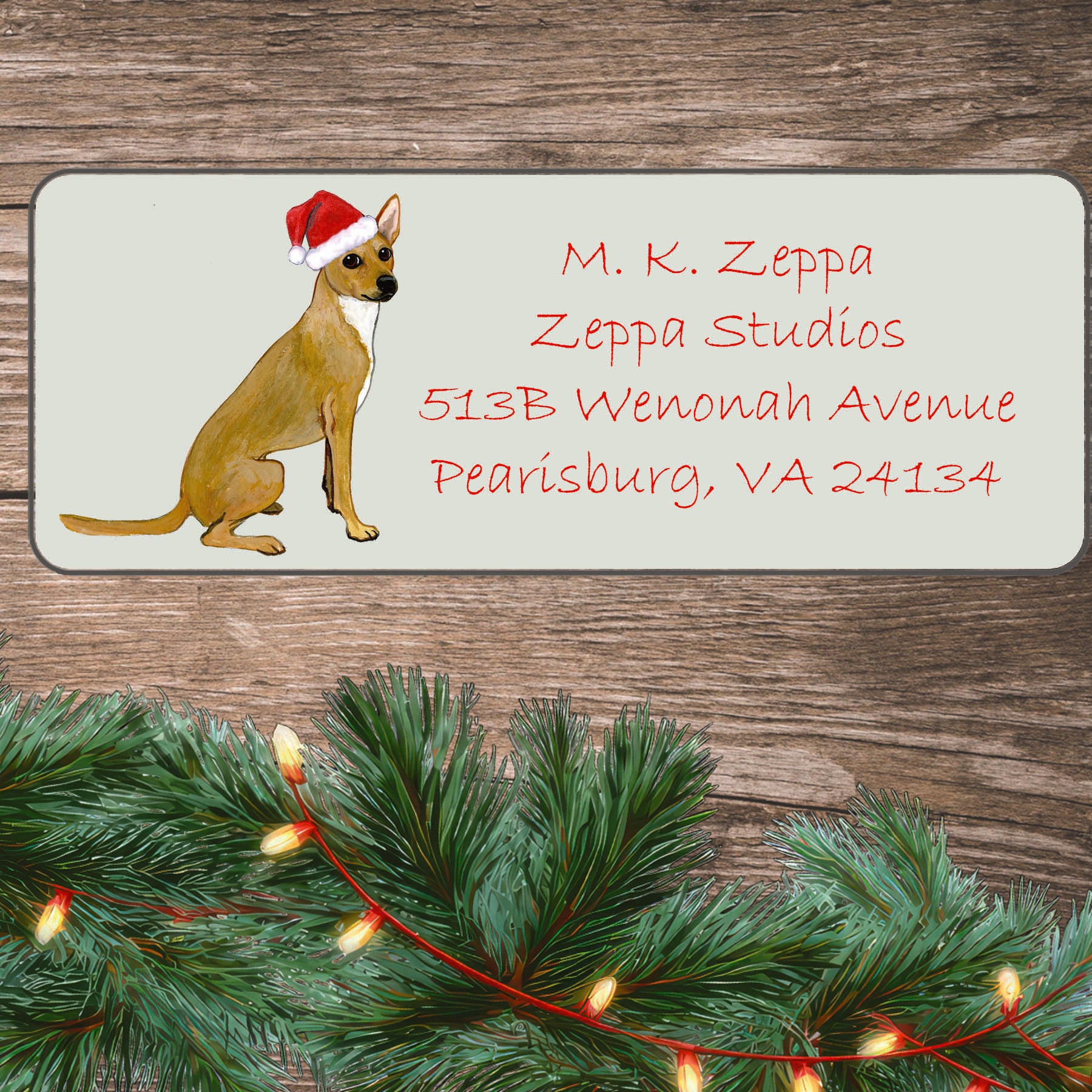 An illustration of a coated Xoloitzcuintli wearing a Santa Hat on an ivory return address label set off by a wood surface with holiday greenery background.