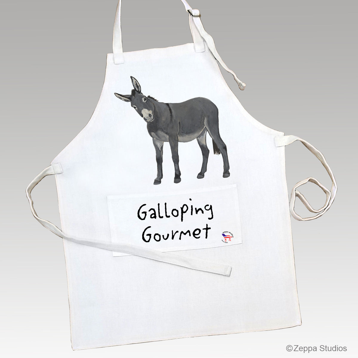 A linen kitchen apron featuring a printed illustration of a gray donkey and the text 'Galloping Gourmet' on the front pocket area.