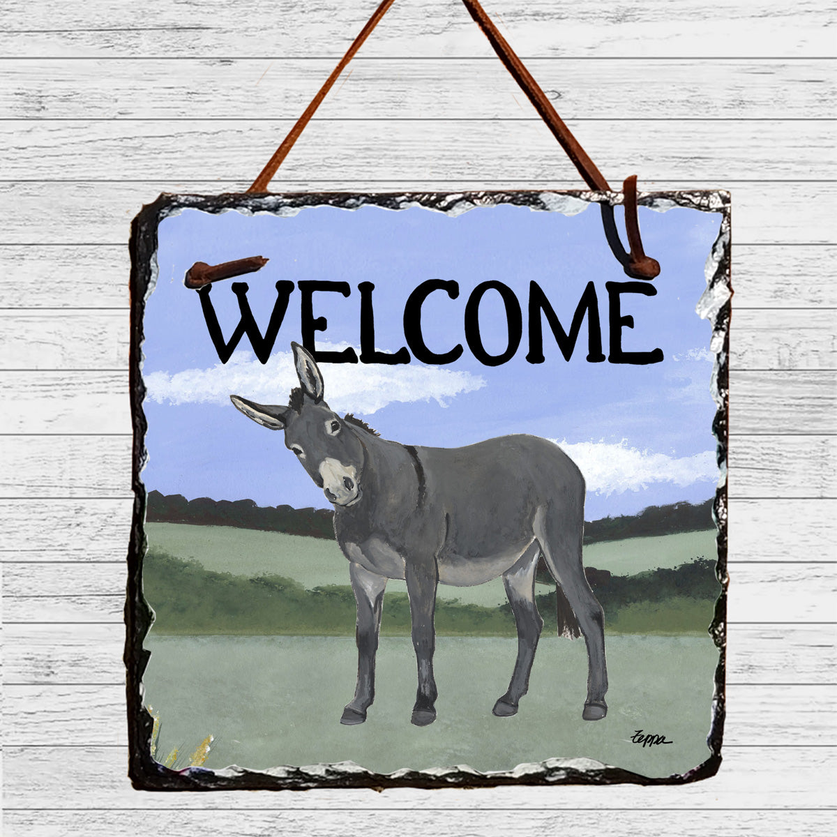 A square slate wall hanging sign with a rustic dark border, hanging by two brown leather straps. The sign features an illustration of a gray donkey standing in a green field under a blue sky, with the word 'WELCOME' in large black letters across the top.