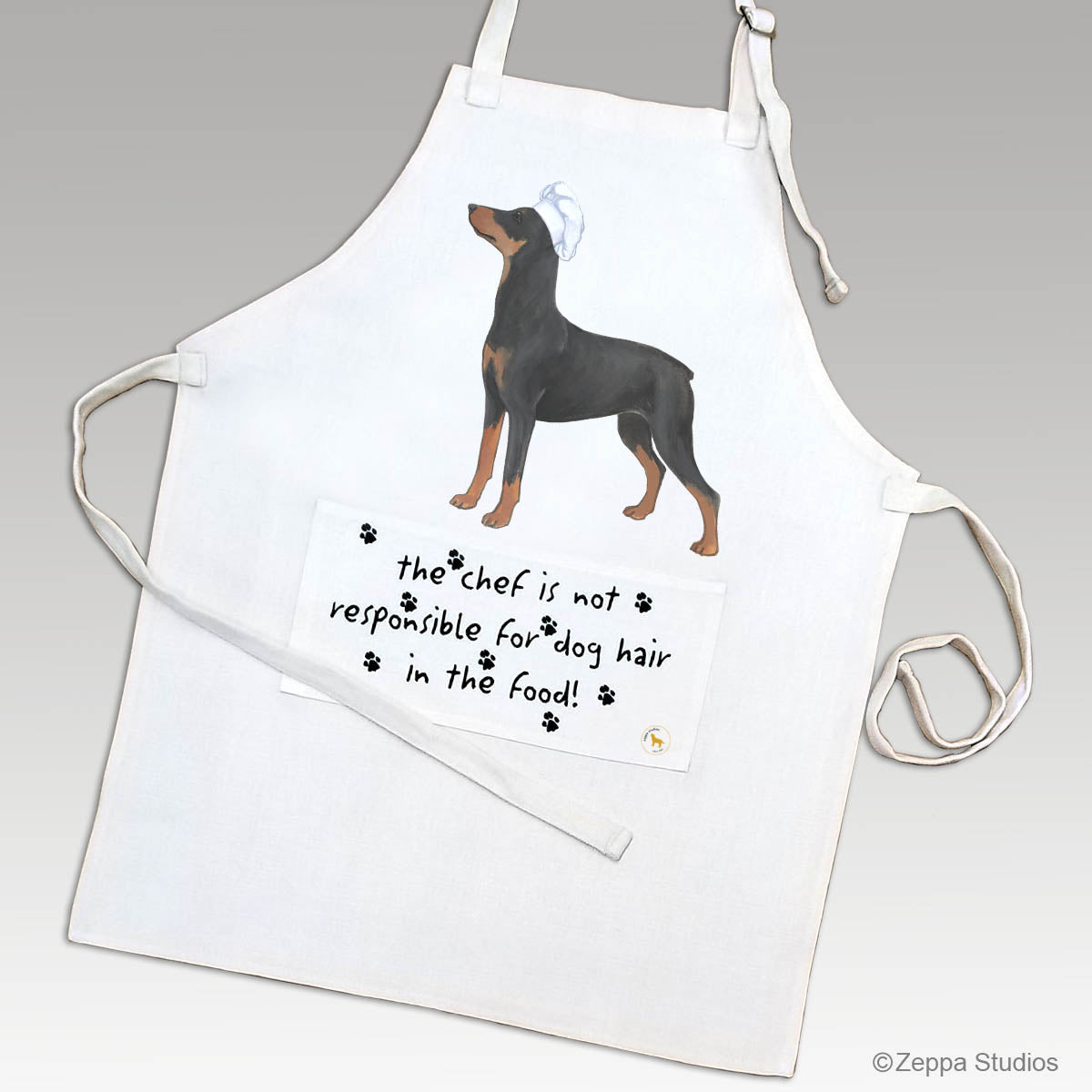 A linen apron featuring a printed illustration of German Pinscher wearing a white chef's hat, with  'the chef is not responsible for dog hair in the food!' on the apron's pocket.