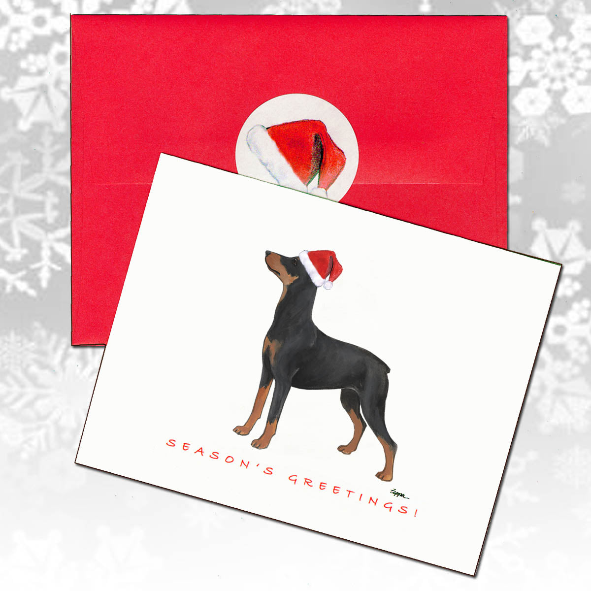 A Christmas greeting card featuring a German Pinscher wearing a Santa hat, with 'SEASON'S GREETINGS!' printed below, shown in front of a red envelope.