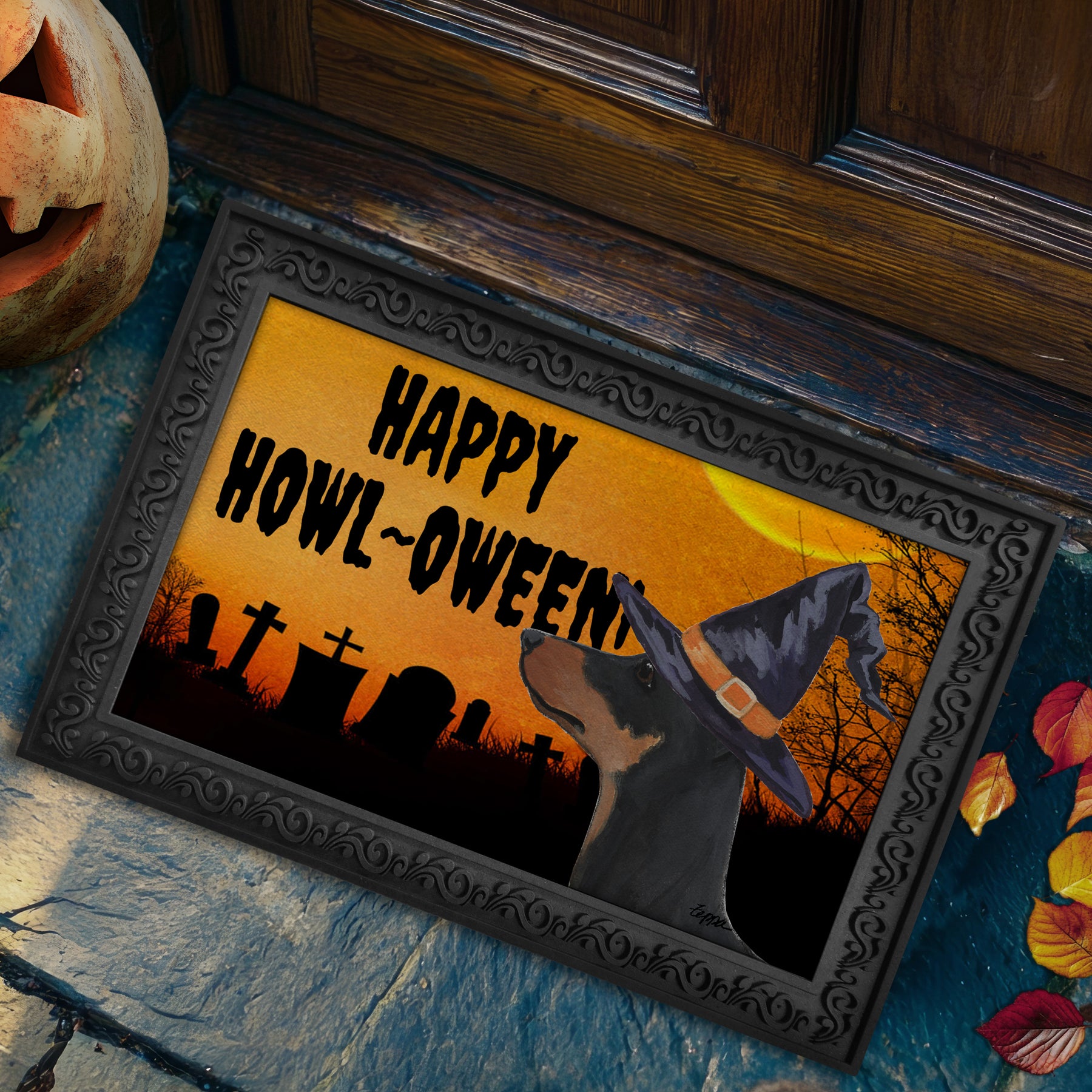 A doormat with an ornate black frame, featuring a German Pinscher in a witch hat against an orange sky with tombstones and the text 'HAPPY HOWL-OWEEN!'. 