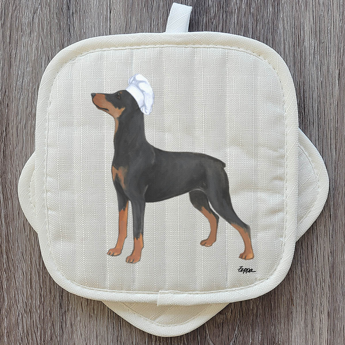 German Pinscher in a chef's hat on a set of potholders.