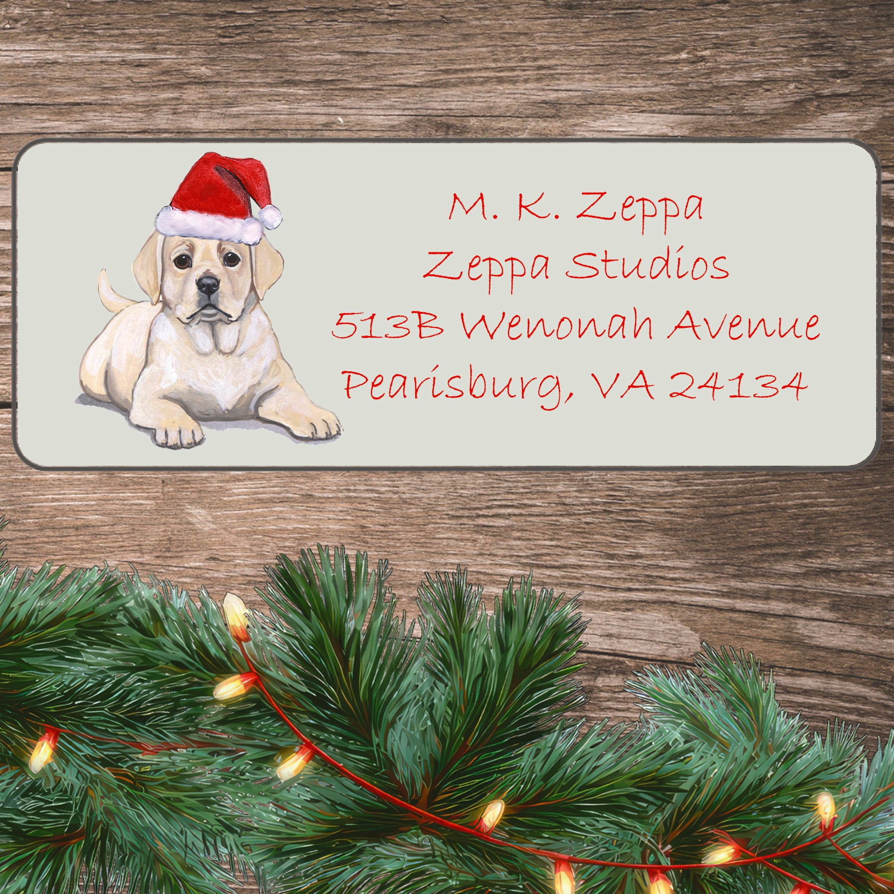 An illustration of a Yellow Lab puppy wearing a Santa Hat on an ivory return address label set off by a wood surface with holiday greenery background.