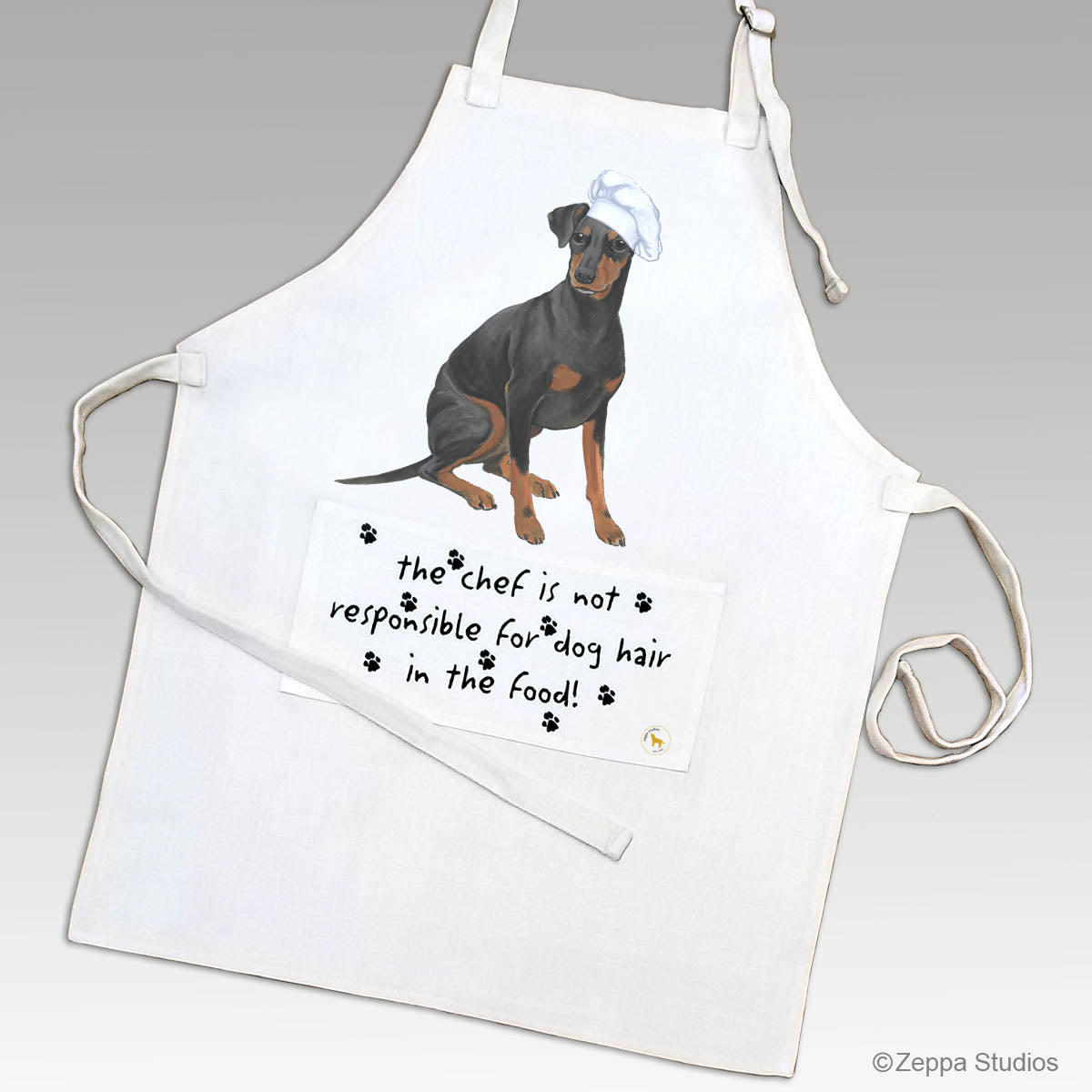 Manchester Terrier in a chef hat on a linen apron with a funny saying on the pocket.