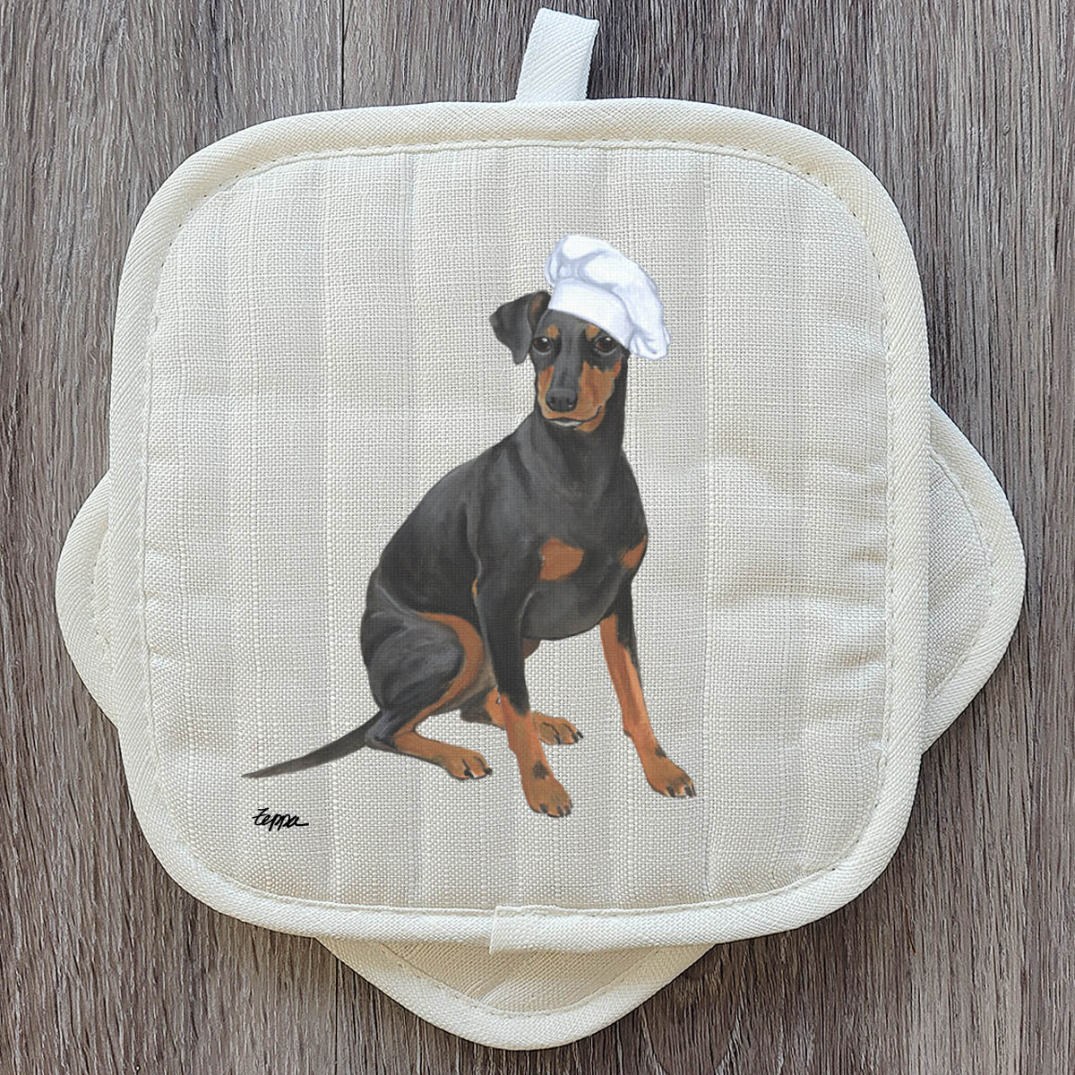 A quilted cream-colored pot holder featuring a printed illustration of a Manchester Terrier wearing a white chef's hat.