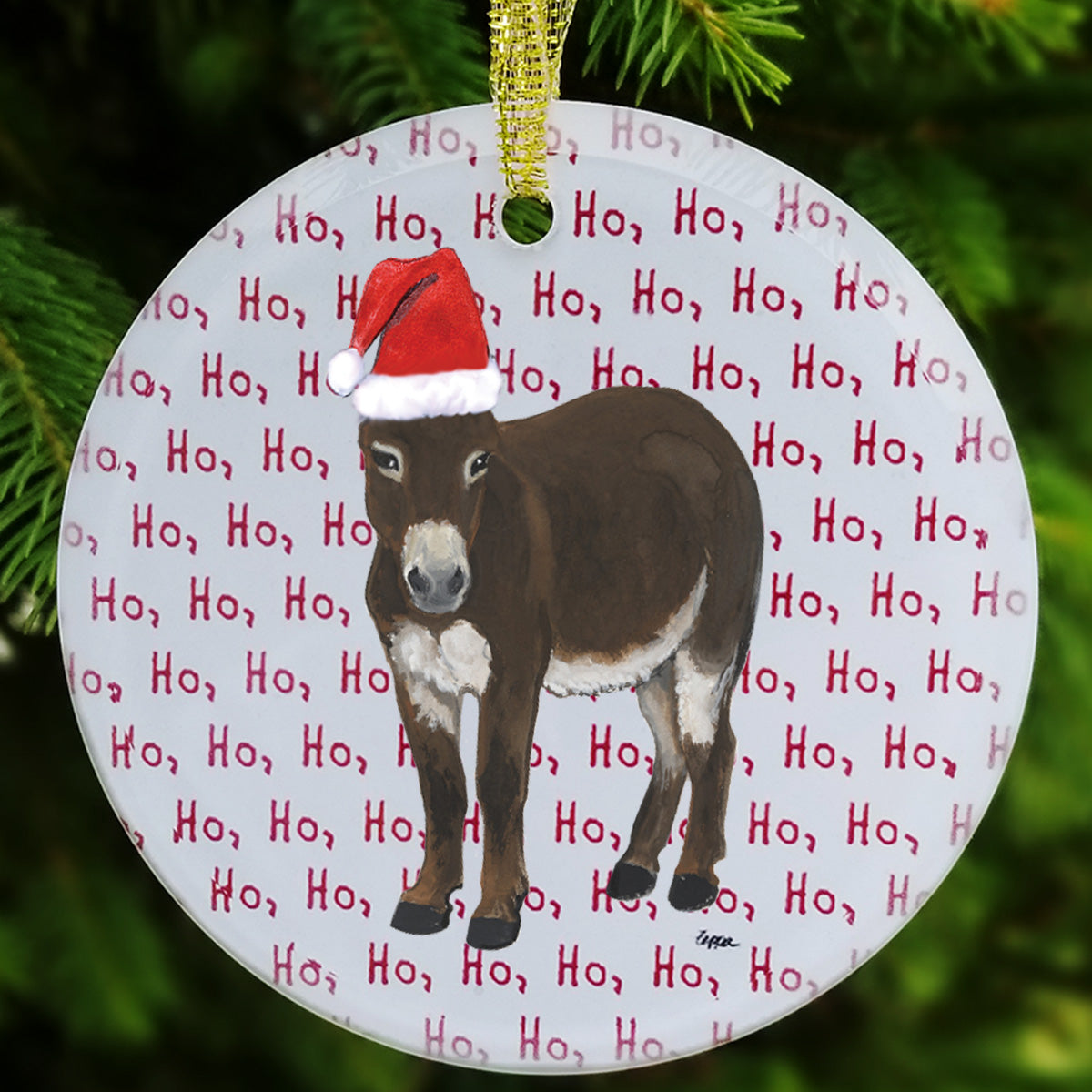 Round glass Christmas ornament featuring an illustration of a brown donkey wearing a red Santa hat, set against a white background with repeated red 'Ho, Ho, Ho' text, hanging from a gold string in front of green pine branches.
